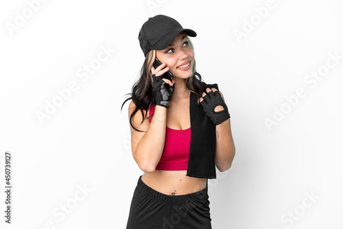 Sport Russian girl with hat and towel isolated on white background keeping a conversation with the mobile phone with someone © luismolinero