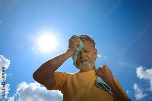 Senior man with towel suffering from heat stroke outdoors, low angle view photo