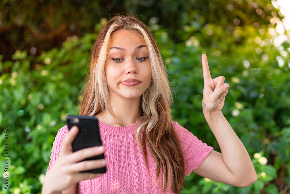 Young pretty woman at outdoors using mobile phone and lifting finger Young pretty woman at outdoors using mobile phone and lifting finger