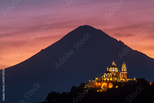 A church on top of a hill with an active volcano behind at dawn