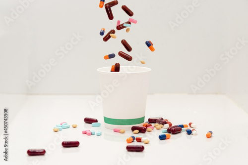 píldoras y pastillas cayendo desde arriba a un vaso de papel con más pastillas y píldoras a su al rededor photo