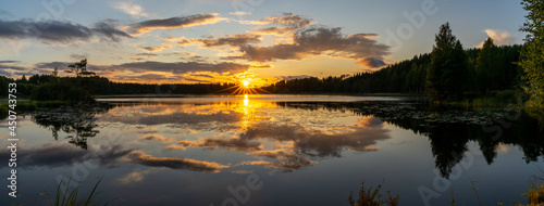 panorama of a colorful sunset reflected in a calm lake landscape with green forest and reeds
