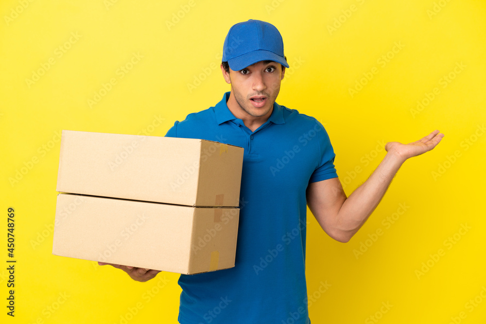 Delivery man over isolated yellow wall having doubts while raising hands Delivery man over isolated yellow wall having doubts while raising hands