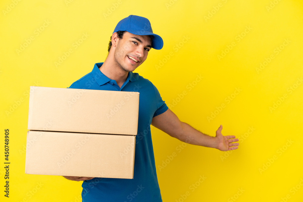 Delivery man over isolated yellow wall extending hands to the side for inviting to come Delivery man over isolated yellow wall extending hands to the side for inviting to come