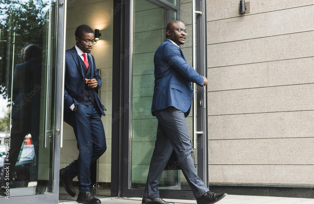two black African American businessman in suits walk out of the building outdoors. two black African American businessman in suits walk out of the building outdoors.