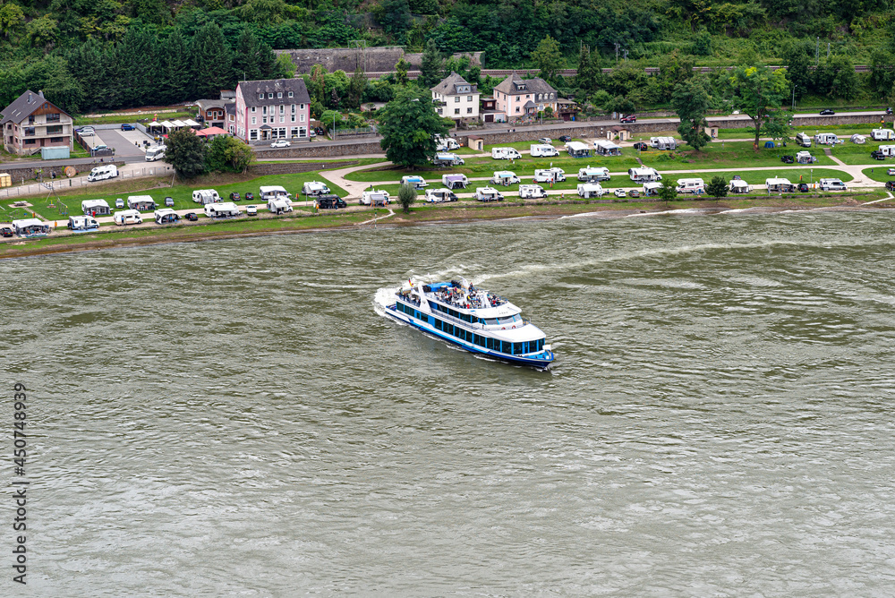 Obraz premium A tourist ship sailing on the river Rhine in western Germany, visible buildings and caravans on the river bank.