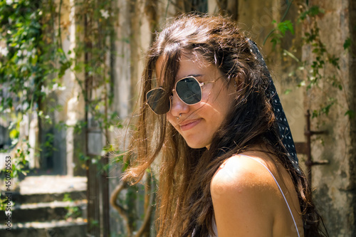 Smiling summer woman with a black scarf hair tie and vintage sunglasses. Portrait of a pretty young girl wearing sunglasses outside on sunny day. Caucasian fashionable female with long brown hair.