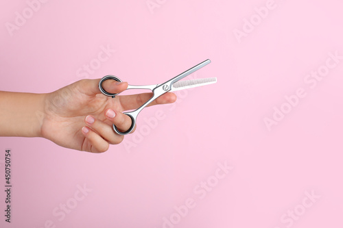 Photography Hairdresser holding professional thinning scissors and space for text on pink background, closeup