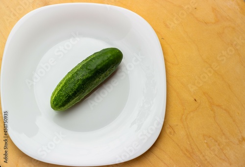 
Green ripe cucumber on a white glossy plate. Top view and copy space