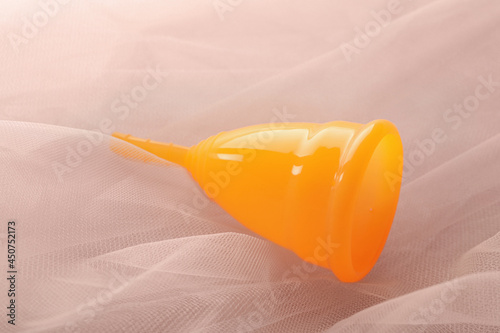 Orange menstrual cup on pink fabric, closeup