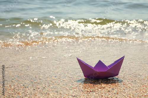 Purple paper boat near sea on sunny day, space for text