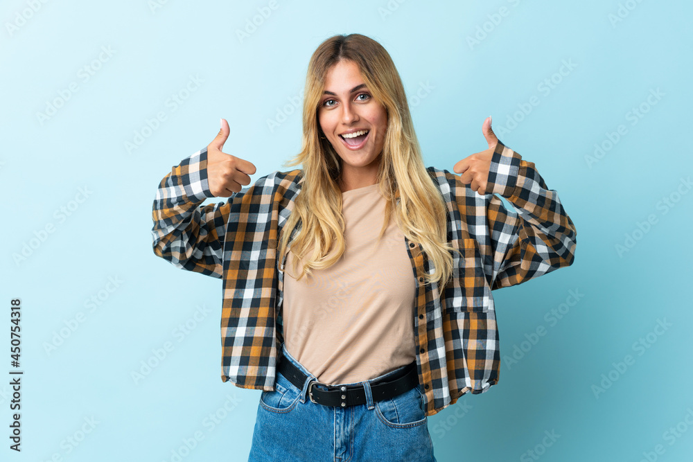 Obraz premium Young blonde Uruguayan isolated on blue background giving a thumbs up gesture