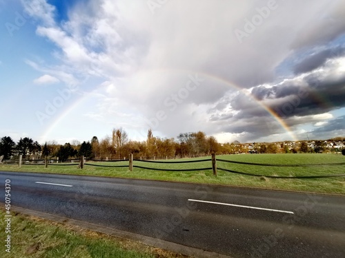 Billede på lærred Rainbow after rain over rural road in countryside with dramatic storm clouds and sunlight