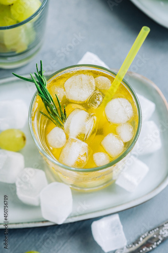 Refreshing summer drink in glass with ice cubes, green grape and rosemary on the table.
