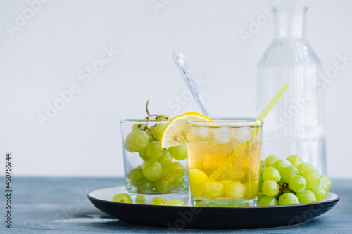 Картината върху платно Refreshing summer drink in glass with ice cubes, green grape and lemon on the table