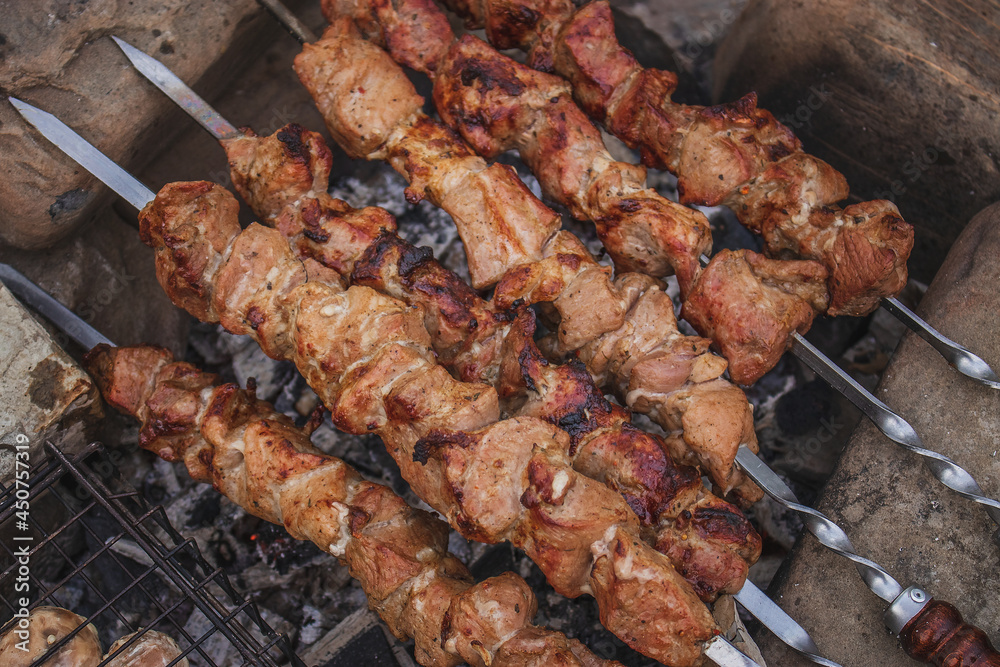 Pieces of meat fried on metal skewers. Cooking shish kebab from raw meat on coals by the fire, in the open air. Pieces of meat and mushrooms are fried in a frying pan.