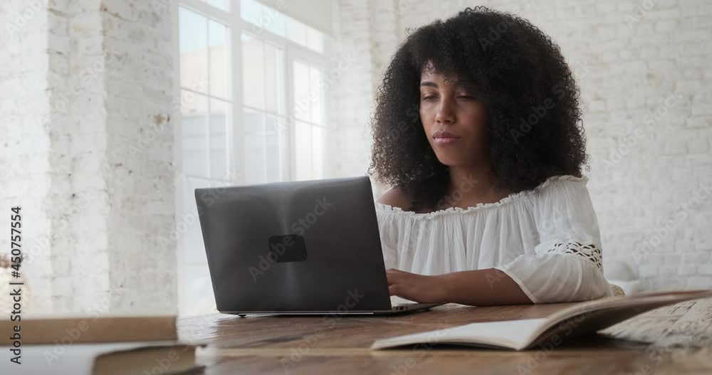 Focused young black woman student preparing for exams using laptop and sitting at table. Concentrated biracial female distant learning foreign languages and working distantly. Focused young black woman student preparing for exams using laptop and sitting at table. Concentrated biracial female distant learning foreign languages and working distantly.