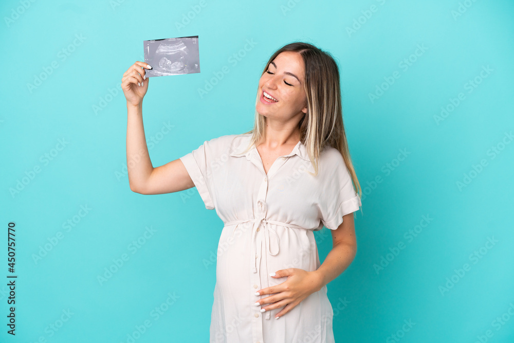 Young Romanian woman isolated on blue background pregnant and holding an ultrasound Young Romanian woman isolated on blue background pregnant and holding an ultrasound