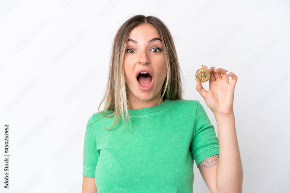 Young Romanian woman holding a Bitcoin isolated on white background with surprise and shocked facial expression Young Romanian woman holding a Bitcoin isolated on white background with surprise and shocked facial expression