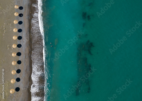 Aerial view from a flying drone of beach umbrellas in a row on an empty beach with braking waves.