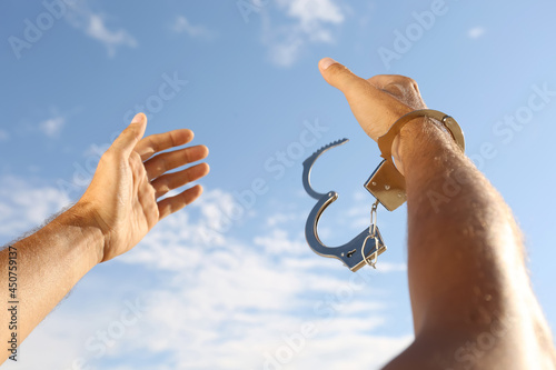 Man in handcuffs against blue sky outdoors, closeup photo