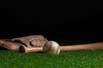 Old baseball bat and mitt low angle on grass field and dark background