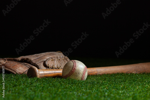Old baseball bat and mitt low angle on grass field and dark background
