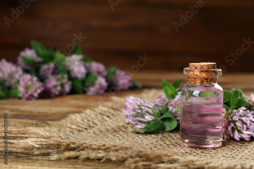 Beautiful clover flowers and bottle of essential oil on wooden table, space for text