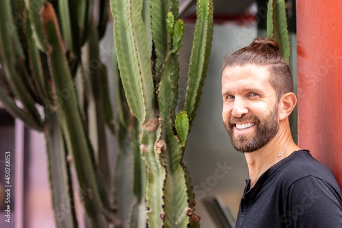 Outdoor portrait of young smiling man in green cactus background.