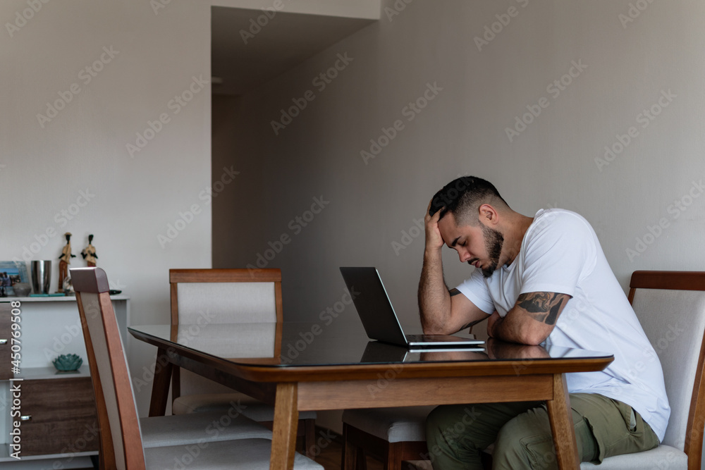 young latin tattooed man in front of laptop stressed out and holding his head young latin tattooed man in front of laptop stressed out and holding his head