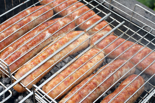 Meat sausages squeezed between grill grates, frying on a grill brazier. Closeup