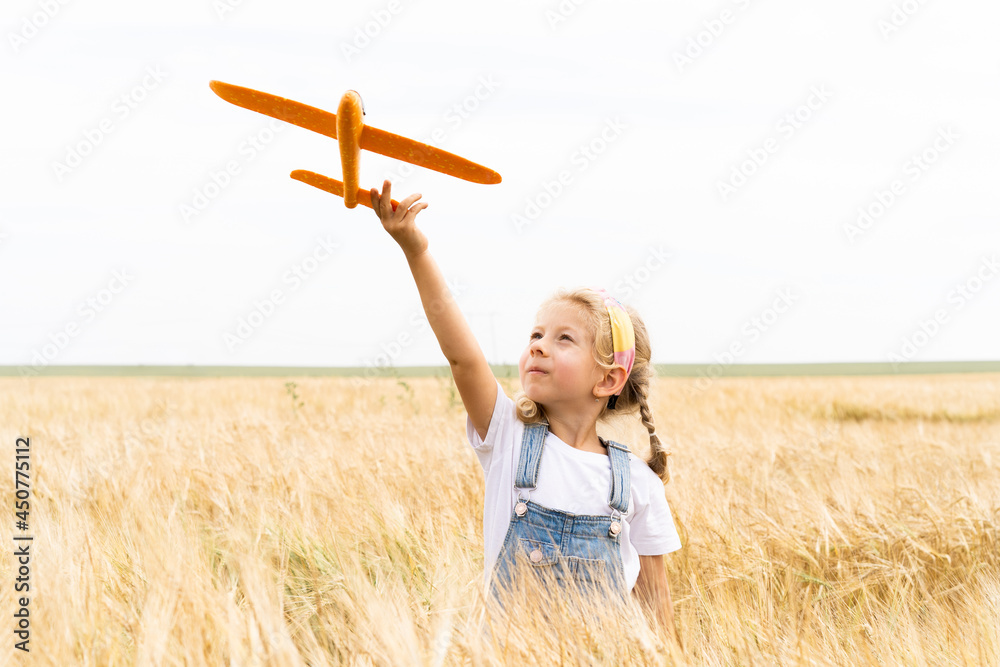 Fototapeta premium Little blonde girl plays plane in the field of rye, grain harvest