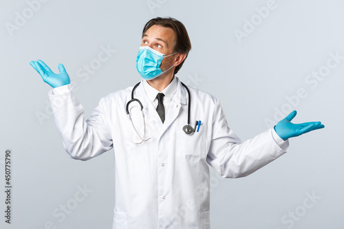 Covid-19, preventing virus, healthcare workers and vaccination concept. Professional male doctor in mask and gloves introduce product, demonstrating medication, looking top left