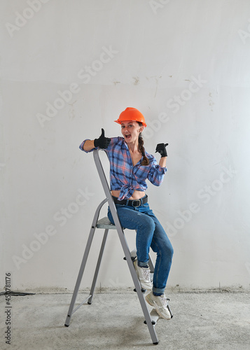 funny girl in hard hat sits on a stepladder