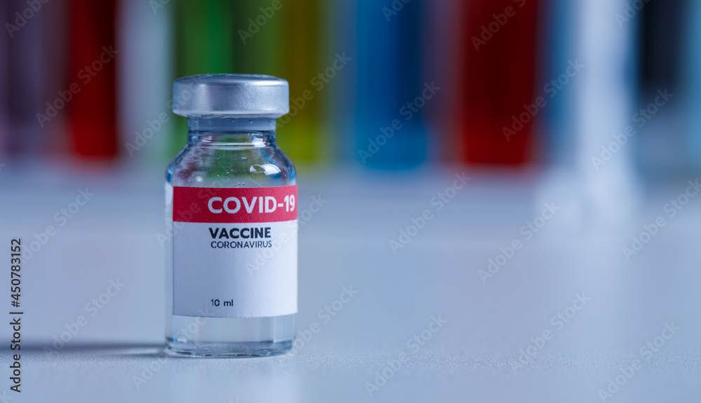 Close up shot of 10 ml coronavirus covid 19 vaccine in small glass vial bottle with red label for protection prevention epidemic pandemic virus outbreak around world in laboratory blurred background