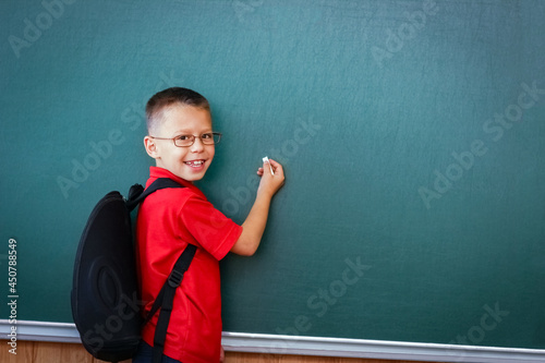A Happy child child standing at the blackboard with a school backpack wearing glasses © Kostia