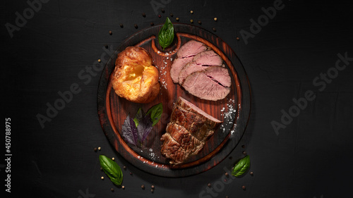 Roastbeef, yorkshire puddnings, basil leaves on a wooden cutting bords .