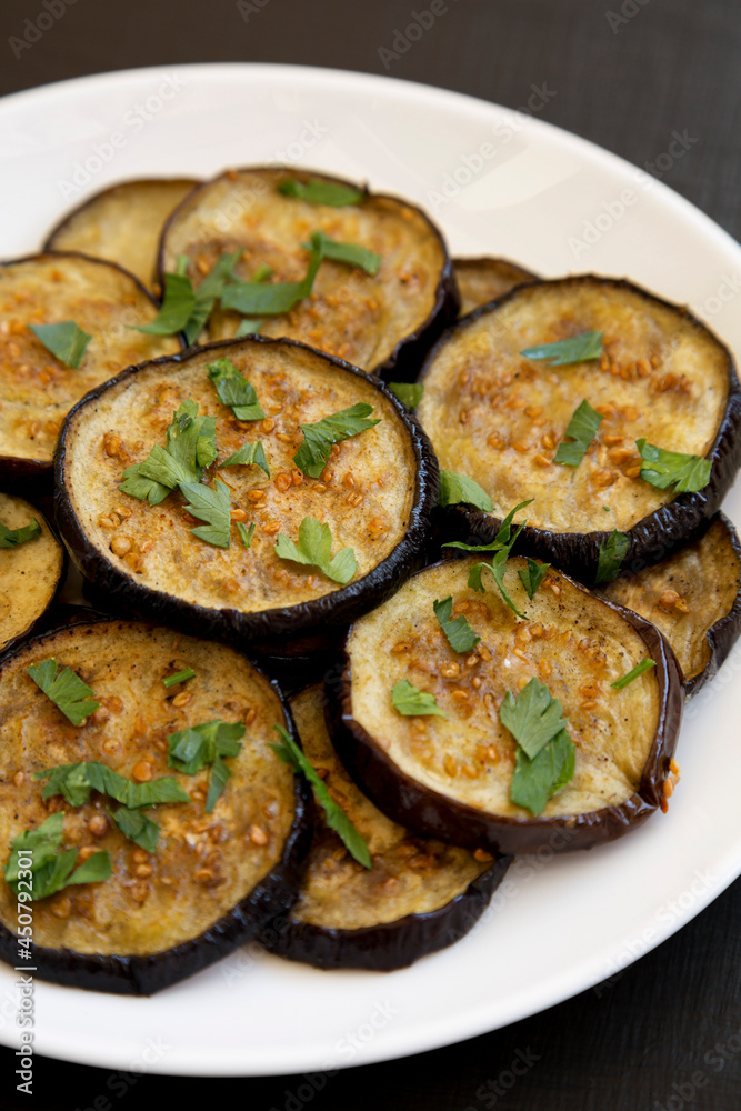 Homemade Organic Roasted Eggplant on a white plate on a black background, side view. Close-up.