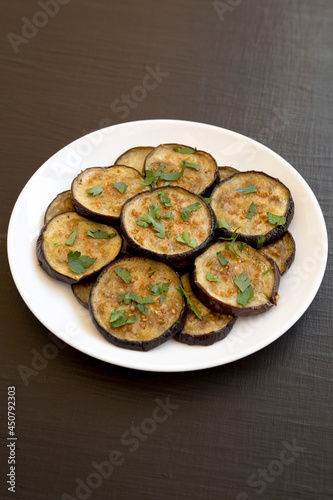 Homemade Organic Roasted Eggplant on a white plate on a black surface, side view.