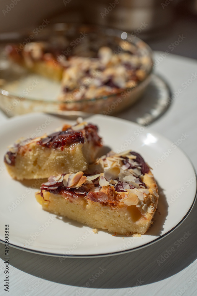 Sliced plum-marzipan pie on a white wooden table. Almond on top.