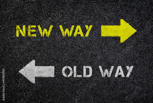 "New way" and "old way" signs/texts with arrows pointing on opposite directions on dark, wet black asphalt road, top view. High resolution full frame textured background, viewed from above.