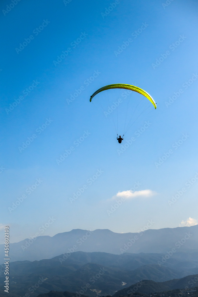 A yellow paraglider is flying over the mountain A yellow paraglider is flying over the mountain