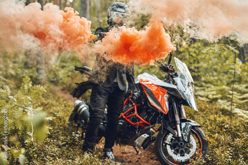 Motorcyclist with colorful smoke going from his hand in forest