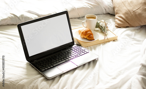 an open laptop with a cup of tea lying on a white bed. breakfast in bed with a laptop with a cup of coffee and a croissant