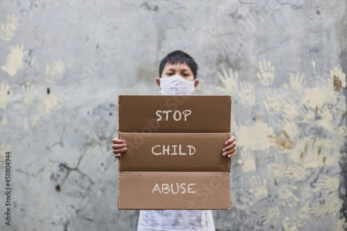 Asian boy in medical mask holding letter board says Stop Child Abuse when campaign with hand print in the cement wall background