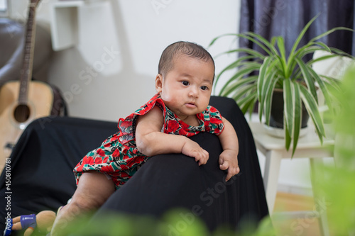 5 months old baby girl leaning and standing on black sofa chair, looking away. 