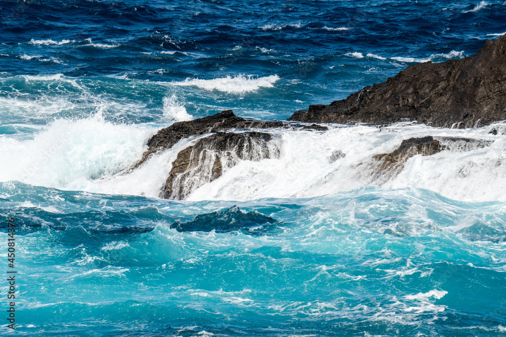 Fototapeta premium Atlantik ocean rollers breaking on black lava rocks at the north coast of Madeira in front of the promenade of Porto Moniz