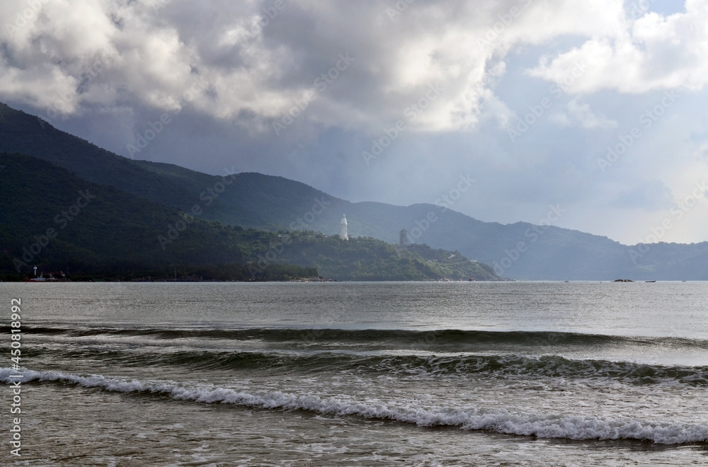 A bay with a hilly shore, on which a statue of Buddha and a small pagoda are visible