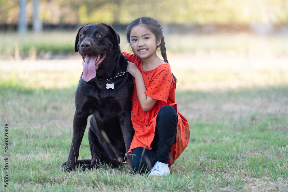 A lovely Southeast Asian child girl in red outfits plays with her big dog in the back or front yard in the evening. Pet lover concept A lovely Southeast Asian child girl in red outfits plays with her big dog in the back or front yard in the evening. Pet lover concept