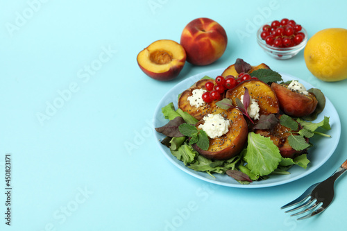 Plate of salad with grilled peach on blue background
